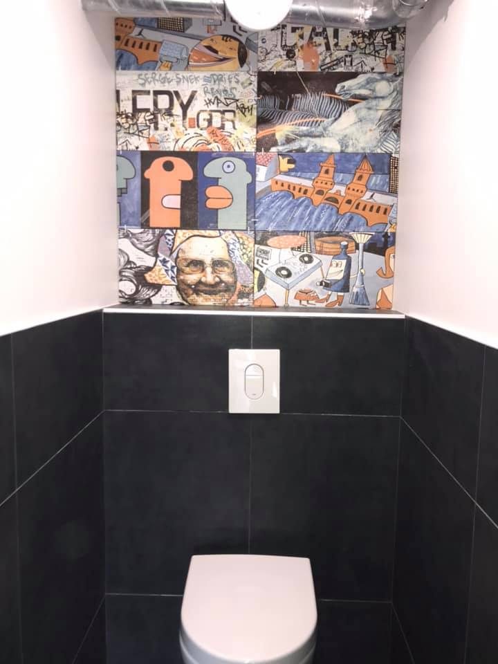 Toilettes : carrelage noir en bas, faïence street-art en haut